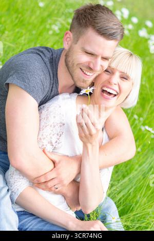 Un couple amoureux s'assoit joyeusement dans un pré avec des marguerites. Banque D'Images