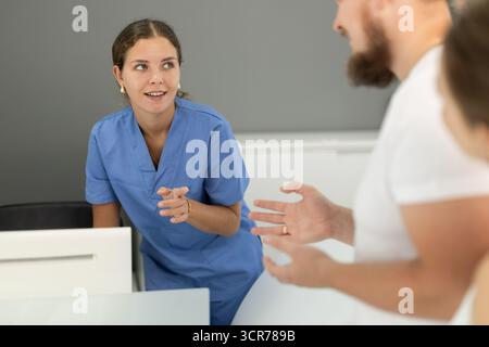 L'homme se tient près de la réception et pose des questions à l'administrateur de la dentisterie Banque D'Images