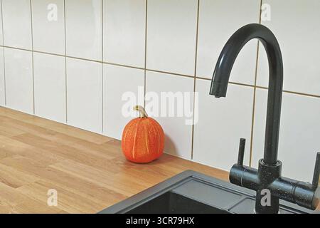Cuisine minimaliste avec robinet noir et petite citrouille sur comptoir en bois contre carreaux blancs Banque D'Images