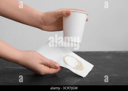 Femme essuyant le café renversé avec une serviette en papier sur la table noire grunge Banque D'Images