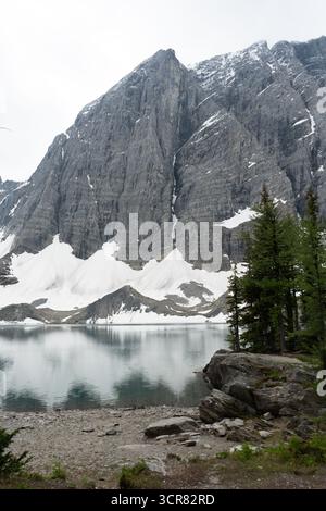 Un lac réfléchissant se trouve devant une montagne massive et accidentée, partiellement couverte de neige Banque D'Images