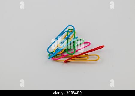 Une collection de trombones colorés aux teintes vives se trouve sur une surface blanche unie. L'arrangement met en valeur les différentes formes et couleurs vibrantes de Banque D'Images