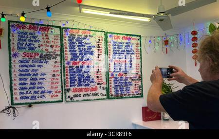 Homme utilisant un smartphone pour prendre une photo du menu mural dans un restaurant chinois, Cairns, Queensland, Australie. Pas DE MR ou PR Banque D'Images