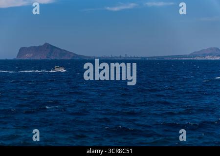Bateau à moteur naviguant sur la mer bleue calme, en arrière-plan Benidorm & Altea Banque D'Images