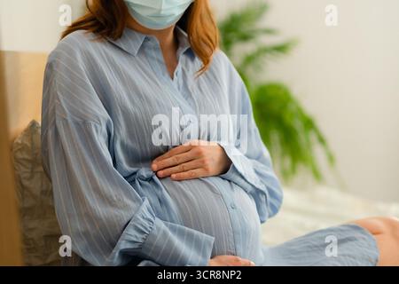 Future mère portant un masque de protection au repos au lit. Gérer les symptômes de la maladie de manière responsable pendant la grossesse. Banque D'Images
