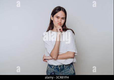 Jeune femme asiatique pose soigneusement avec une main sur son menton dans un cadre de studio simple Banque D'Images