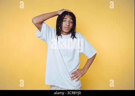 Jeune homme pose avec une expression réfléchie sur un fond jaune vif tout en portant des vêtements décontractés Banque D'Images
