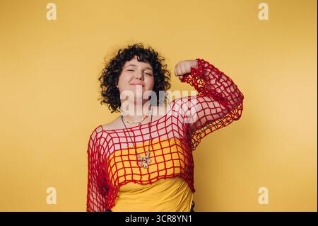 Jeune femme confiante prend la pose sur un fond jaune vif tout en portant une tenue colorée et une expression ludique Banque D'Images