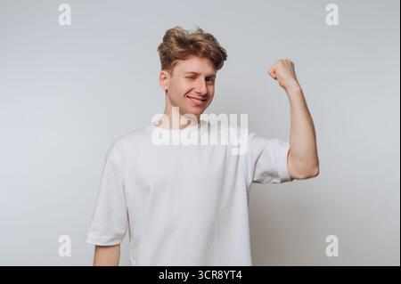 Jeune homme montrant la force et la confiance tout en faisant un clin d'œil sur un fond simple Banque D'Images