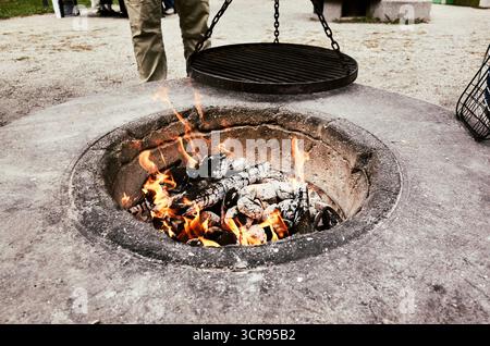 Le feu brûle dans un foyer de ciment. Une personne tient un anneau métallique au-dessus du feu Banque D'Images