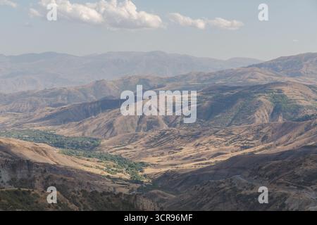 Vue sur les chaînes de montagnes escarpées sous un ciel brumeux, avec des pentes dorées contrastant avec des parcelles de végétation verte, col de Vardenyats, Arménie. Banque D'Images