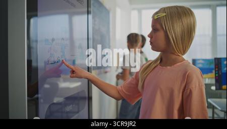 Gros plan de belle écolière européenne travaillant sur grand écran numérique pendant la leçon dans la salle de classe lumineuse et moderne. Outils AI dans le système éducatif moderne. Concept de STEM Education. Tir statique. Banque D'Images