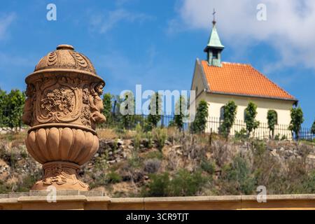 Vase ornemental en pierre et pittoresque petite église sur la colline contre le ciel bleu d'été, Prague, Tchéquie Banque D'Images