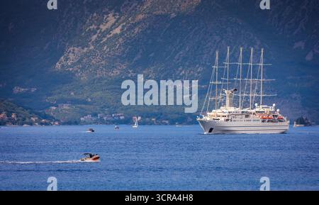 Yacht à voile blanc entrant dans la baie de Kotor au Monténégro avec des montagnes spectaculaires en arrière-plan Banque D'Images