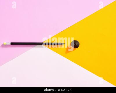 Crayon noir et copeaux disposés sur un fond géométrique rose, blanc et jaune éclatant, formant une composition d'art contemporain Banque D'Images
