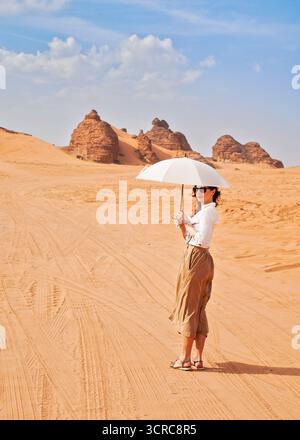 Jeune femme, lunettes de soleil, henné temporaire sur sa main, avec parapluie blanc contre le soleil marchant dans le désert d'Alula Banque D'Images