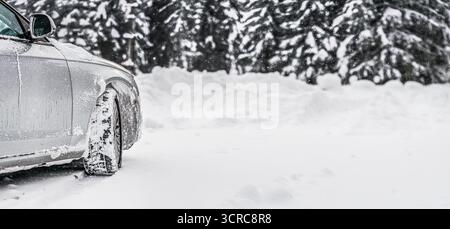 Voiture argentée couverte de glace garée sur la route de neige, vue de détail sur le côté et la roue avant de derrière, arbres flous arrière-plan espace vide pour le texte à droite Banque D'Images