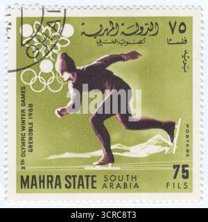 YÉMEN, Mahra - 1967 : 75 fils timbre-poste représentant Speed ​​Skating, un sport de compétition où les athlètes courent sur patins à glace. Il comporte deux disciplines principales. Patinage de vitesse sur longue piste, les patineurs courent sur une piste ovale de 400 M. Dans les épreuves individuelles, deux patineurs courent contre la montre dans des couloirs séparés, changeant de couloirs sur le dos droit pour égaliser la distance. Patinage de vitesse sur piste courte, plusieurs patineurs courent simultanément sur une patinoire plus petite, de la taille d'une patinoire de hockey. C'est un événement de style pack avec des manches, où la position compte pour avancer à la finale. Jeux Olympiques d'hiver 1968, Grenoble Banque D'Images