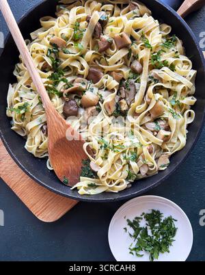 Cuisine italienne. Tagliatelle aux champignons porcini et persil dans une poêle sur fond sombre. Plat d'automne fait maison. Vue de dessus. Banque D'Images