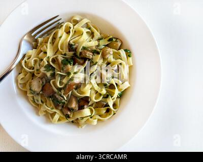 Cuisine italienne. Tagliatelle aux champignons porcini et persil dans une assiette blanche sur une table blanche. Plat d'automne fait maison. Vue de dessus. Banque D'Images