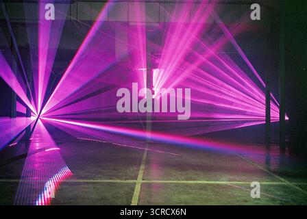 Photo de film analogique de faisceaux lumineux rouges et violets coupant à travers la brume dans un ensemble de garage. Les lasers s'étendent vers la caméra - surréaliste, graveleux, atmosphérique. Banque D'Images