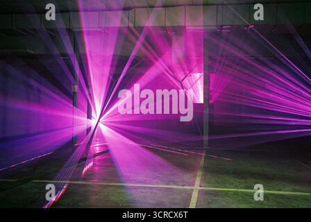 Photo de film analogique de faisceaux lumineux rouges et violets coupant à travers la brume dans un ensemble de garage. Les lasers s'étendent vers la caméra - surréaliste, graveleux, atmosphérique. Banque D'Images