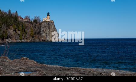 Eau bleue du lac supérieur et ciel bleu clair, avec le phare de Split Rock au sommet de la falaise rocheuse, lors d'une belle journée de printemps dans le Minnesota. Banque D'Images