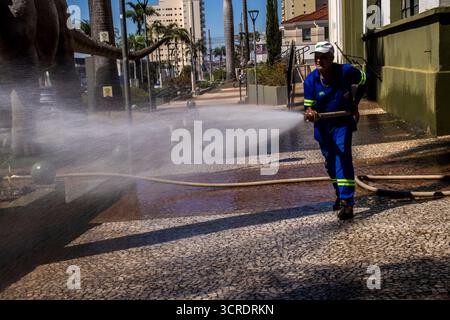 Marilia, SP, Brésil, 10 septembre 2025. Travailleur lavant le trottoir avec un tuyau devant le musée de paléontologie dans le centre-ville, soulignant ur Banque D'Images
