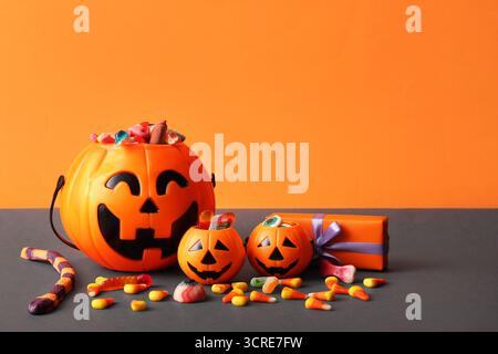 Chaudrons en forme de citrouille avec des bonbons pour Halloween et boîte cadeau sur fond orange Banque D'Images