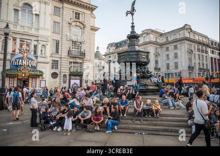 Les touristes s'assoient sur les marches de la fontaine commémorative Shaftesbury à Piccadilly Circus dans le centre-ville de Londres au crépuscule. Banque D'Images