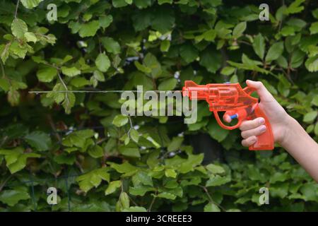 Un enfant tient un pistolet jouet qui tire de l'eau. Gros plan d'un pistolet à eau dans la main d'un enfant tirant un jet d'eau. Banque D'Images