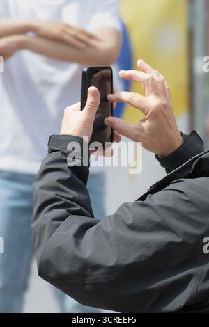 Mains d'un homme âgé filmant une performance d'événement sur un smartphone Banque D'Images