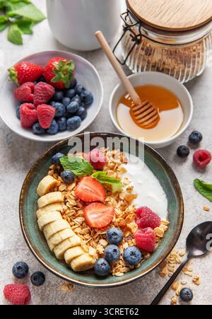 Bol de petit déjeuner sain plein de granola, yaourt, tranches de banane, fraises, bleuets, et les framboises, offrant un début vibrant et nutritif Banque D'Images
