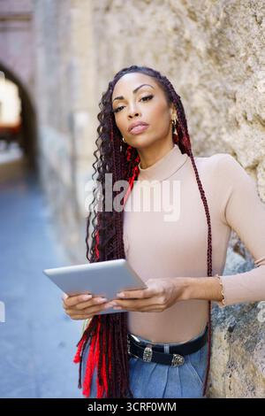 Une femme confiante tenant une tablette dans un cadre urbain dynamique lors d'une belle journée Banque D'Images