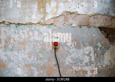 Vieux mur altéré avec de la peinture écaillée, des briques apparentes et un interrupteur rouge vintage. Textures rustiques et détails de décomposition créent un industriel, urbain Banque D'Images