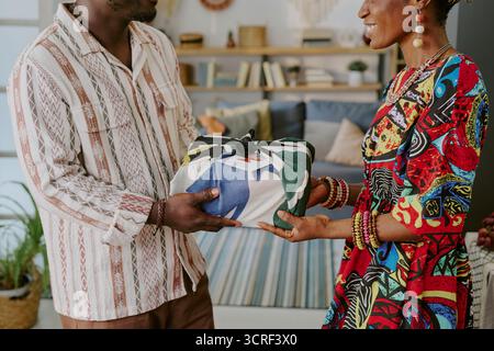 Jeune homme noir adulte donnant cadeau emballé à jeune femme noire adulte souriant Banque D'Images