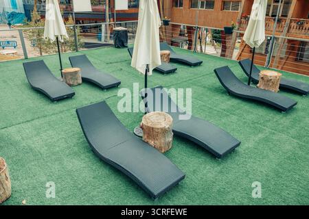 Coin salon avec chaises longues noires et parasols blancs sur une pelouse verte. Les bâtiments environnants sont visibles, créant une atmosphère récréative dans un Banque D'Images