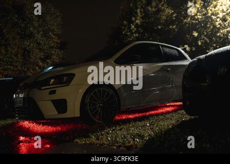 Rome, italie 30 septembre 2025 : volkswagen polo gti, modifié avec des roues personnalisées et un effet d'éclairage rouge sous lueur saisissant, assis sur l'herbe humide durin Banque D'Images