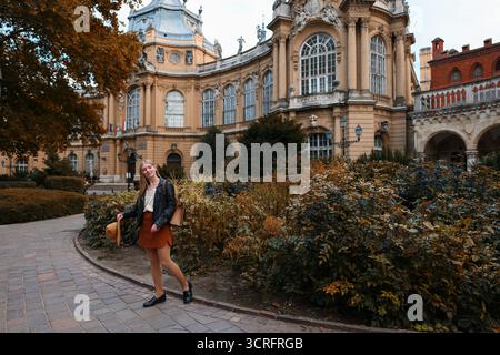 Voyage de ville d'automne, touriste féminine avec sac à dos regardant en arrière près de monument historique. Banque D'Images