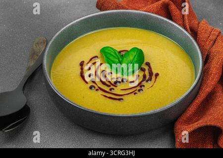 Soupe crémeuse à la courge pattypan, garnie de basilic et de glaçage balsamique, servie dans un bol tendance avec des ingrédients frais et des épices. Béton de pierre sombre b Banque D'Images