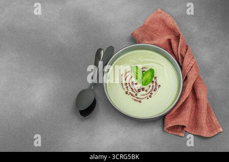 Soupe crémeuse à la courge pattypan, garnie de basilic et de glaçage balsamique, servie dans un bol tendance avec des ingrédients frais et des épices. Béton de pierre sombre b Banque D'Images
