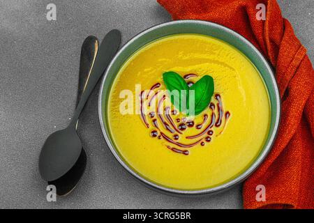 Soupe crémeuse à la courge pattypan, garnie de basilic et de glaçage balsamique, servie dans un bol tendance avec des ingrédients frais et des épices. Béton de pierre sombre b Banque D'Images