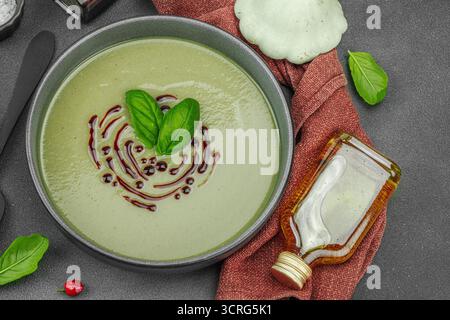 Soupe crémeuse à la courge pattypan, garnie de basilic et de glaçage balsamique, servie dans un bol tendance avec des ingrédients frais et des épices. Béton de pierre sombre b Banque D'Images