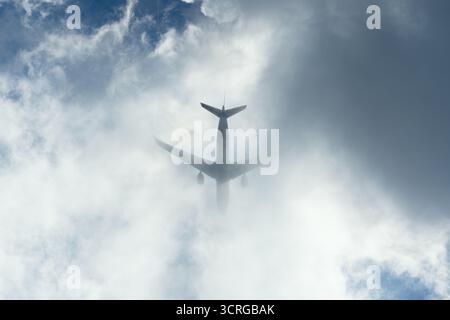 Silhouette d'un avion disparaissant dans des nuages dramatiques, vue d'en bas. Banque D'Images