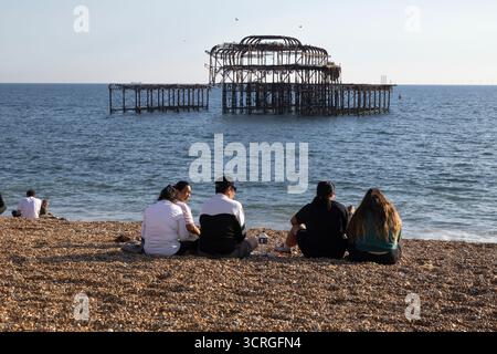 Les gens assis sur la plage dans le soleil de l'après-midi avec Brighton West Pier derrière, Brighton, East Sussex, Angleterre, Royaume-Uni, Europe Banque D'Images