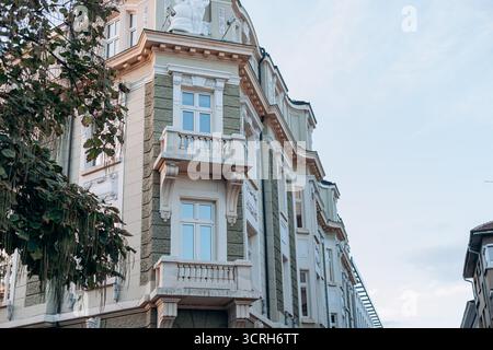 Élégant bâtiment d'angle européen avec sculptures, façade verte et balcons blancs dans l'architecture historique de Sofia. Banque D'Images