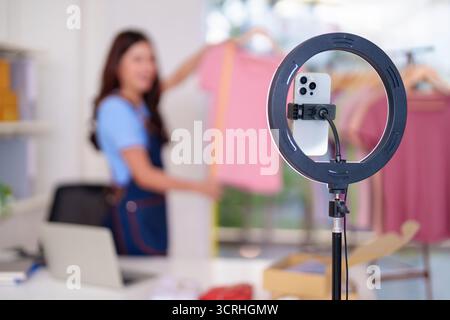 Femme asiatique adulte diffuse en direct les ventes de vêtements de la maison. Entrepreneur présente des vêtements de mode en ligne à l'aide de la configuration de la lumière annulaire de smartphone pour e- Banque D'Images