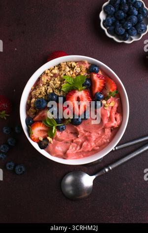 Bol de smoothie à l'açai frais surmonté de fraises, de bleuets et de granola croquant, petit déjeuner végétalien sain. Banque D'Images