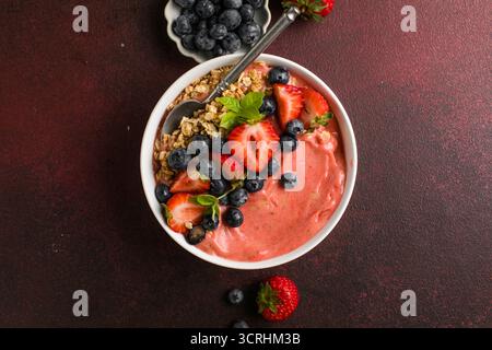 Bol de smoothie à l'açai frais surmonté de fraises, de bleuets et de granola croquant, petit déjeuner végétalien sain. Banque D'Images
