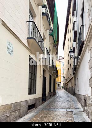 Une rue pavée étroite flanquée de bâtiments avec balcons en fer, menant à un aperçu des façades jaunes ensoleillées au loin, incarnant urbain c Banque D'Images